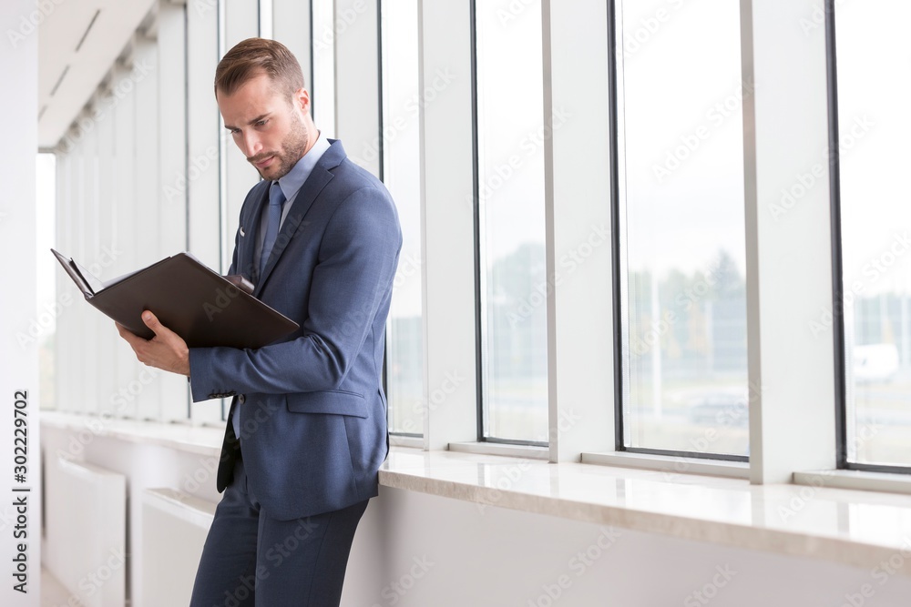 Businessman reading document against window in office Businessman reading document against window in office