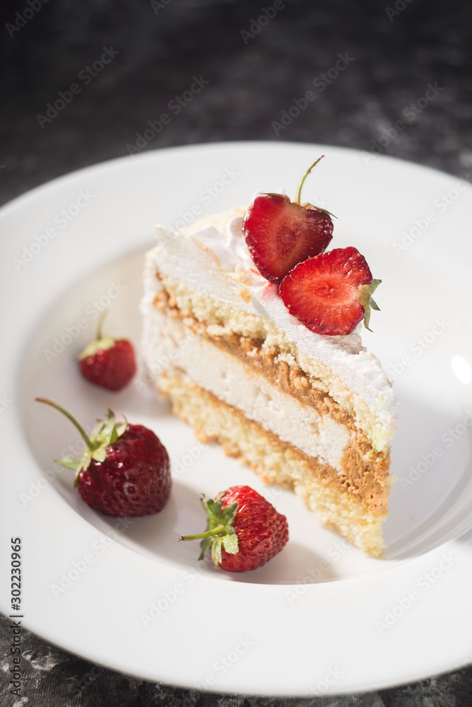 a piece of delicate cake, with slices of sliced strawberries, on a white plate on a white and gray background a piece of delicate cake, with slices of sliced strawberries, on a white plate on a white and gray background