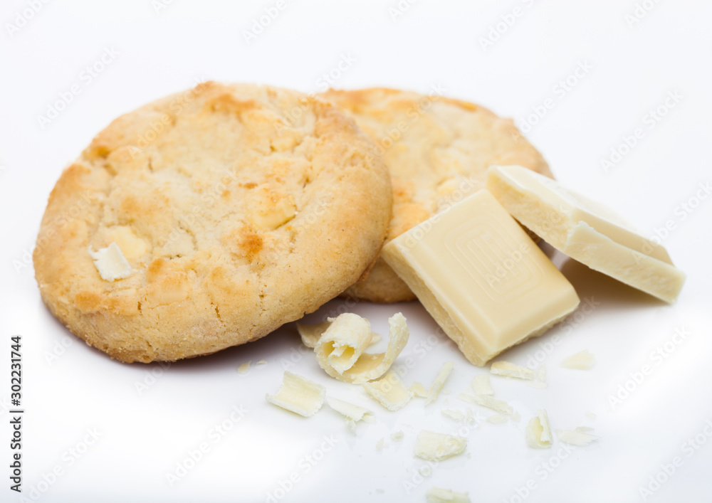White chocolate biscuit cookies with chocolate blocks and curls on white background.
