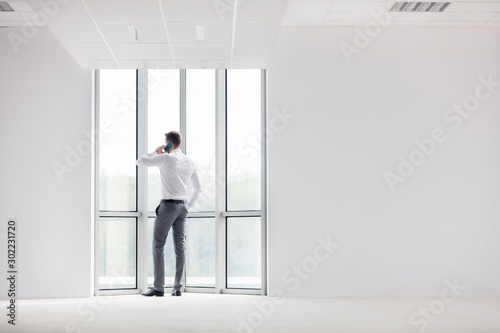 Rear view of businessman standing while talking on smartphone in new office