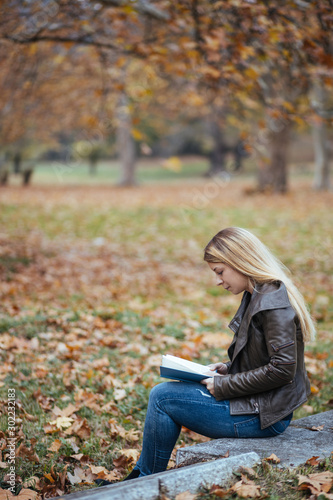 Young woman reading a book in a park in autumn