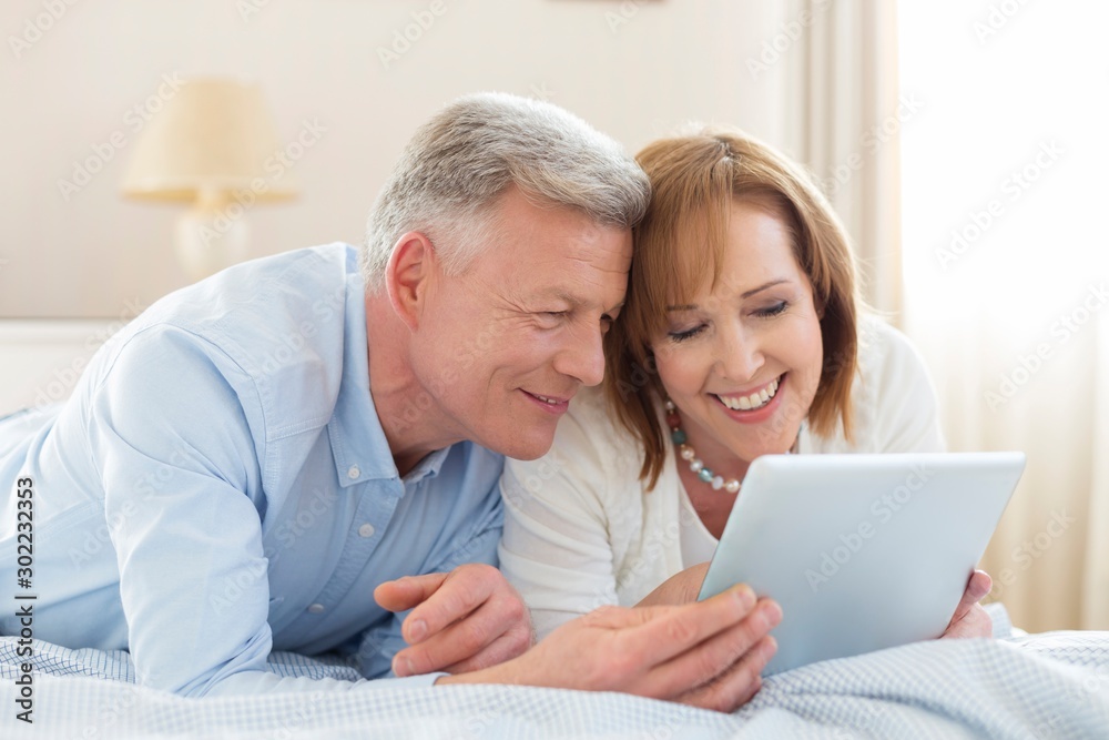 Smiling mature couple sharing digital tablet while lying on bed at home Smiling mature couple sharing digital tablet while lying on bed at home