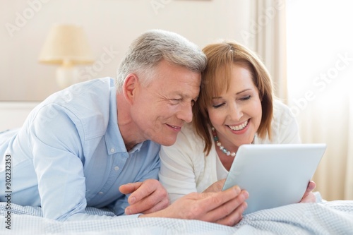 Smiling mature couple sharing digital tablet while lying on bed at home © moodboard