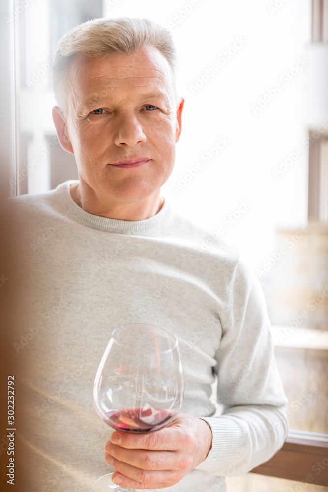 Portrait of mature man holding wineglass standing at home Portrait of mature man holding wineglass standing at home