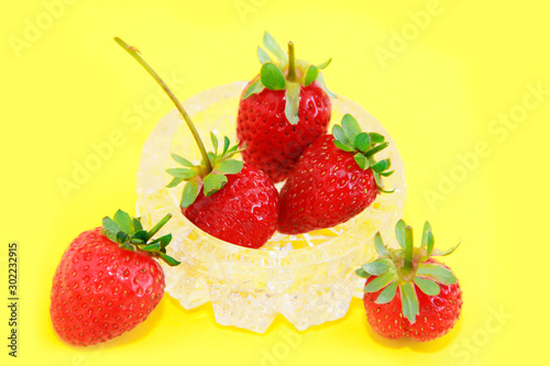 red natural fresh strawberries in a decorative glass plate on a yellow background