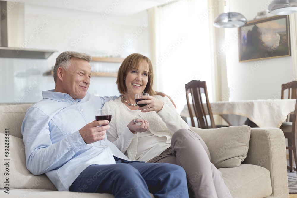 Smiling mature couple sitting on sofa while holding wineglasses at home
