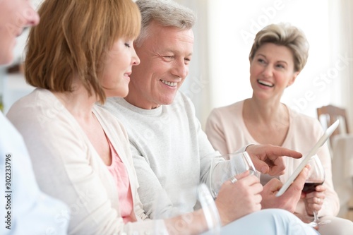 Smiling mature man showing digital tablet to friends at home