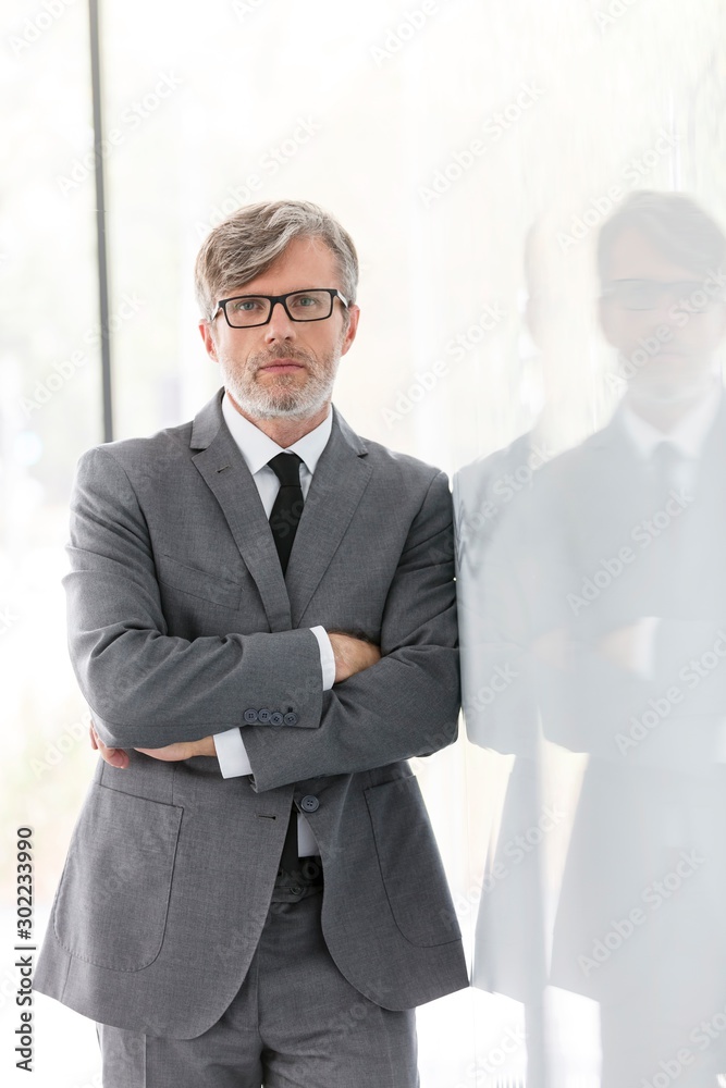Mature confident businessman standing with rms crossed in office Mature confident businessman standing with rms crossed in office