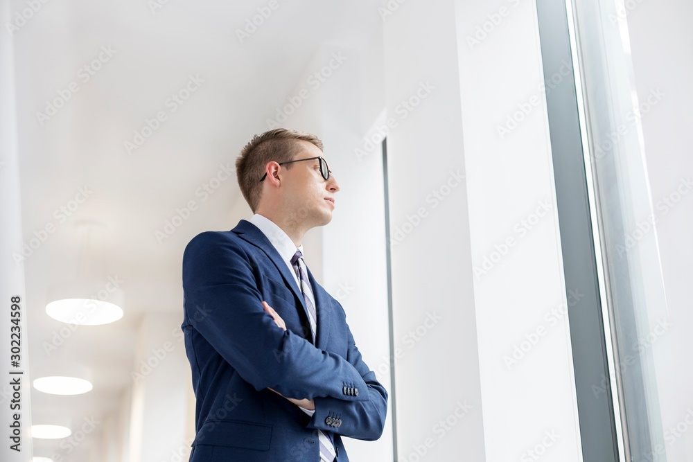 Attractive young thoughtful businessman looking through the window in office