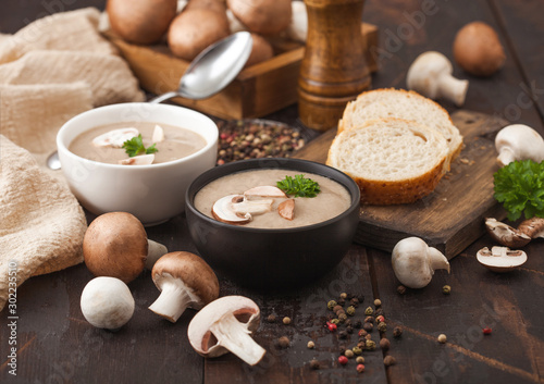 Ceramic bowl plates of creamy chestnut champignon mushroom soup with spoon, pepper and kitchen cloth on dark wooden  background and box of raw mushrooms. photo