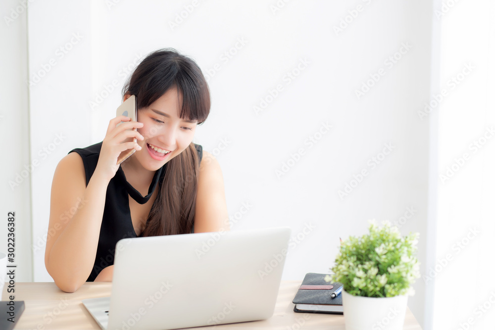 Beautiful young freelance asian woman smiling working on laptop computer and talking mobile smart phone at desk office with professional, girl using notebook, business and lifestyle concept. Beautiful young freelance asian woman smiling working on laptop computer and talking mobile smart phone at desk office with professional, girl using notebook, business and lifestyle concept.