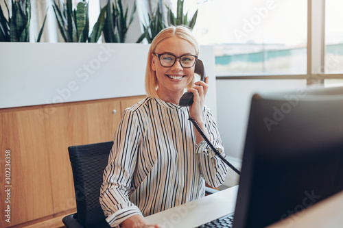 Smiling businesswoman sitting at her desk talking on a telephone photo