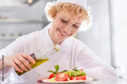 Smiling mature chef pouring oil on salad in plate at restaurant