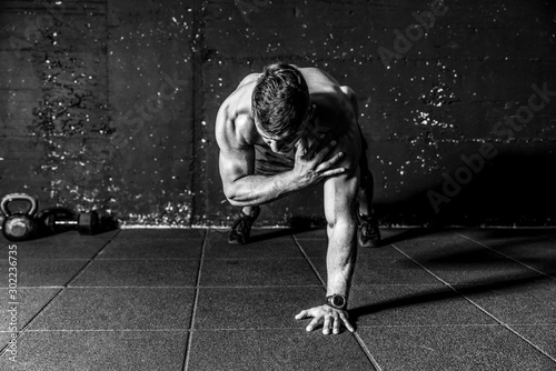 Young sweaty strong and fit muscular man push ups workout with touching his shoulder on one hand in the gym on the floor cross training black and white real people photo
