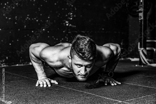 Strong sweaty fit young toned muscular fitness man with big muscles push ups workout cross training on the gym floor black and white photo