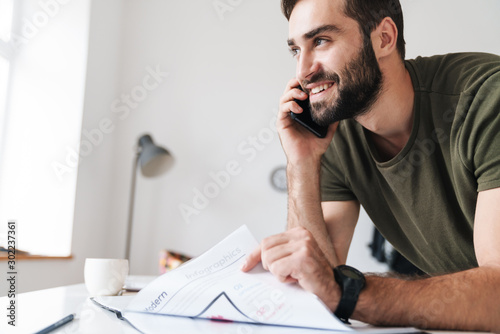 Image of pleased caucasian man reading documents and talking cellphone