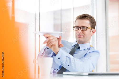 Attractive businessman playing paper plane in office