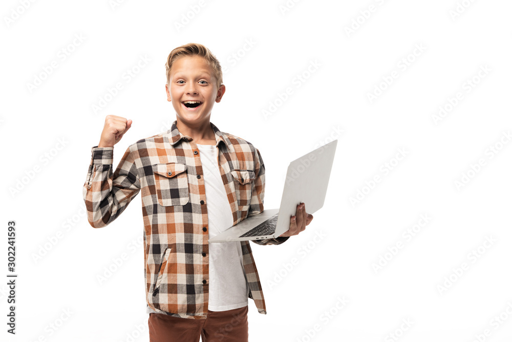 cheerful boy holding laptop, showing winner gesture and looking at camera isolated on white cheerful boy holding laptop, showing winner gesture and looking at camera isolated on white