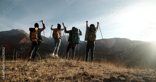 Group of four young people having a hiking tour, going for trekking adventure together, reaching top of mountain and cheering - friendship, achievement concept 4k footage