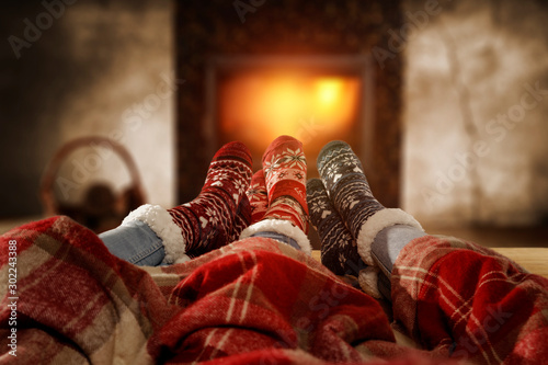 Woolen christmas socks and woman legs on wooden table. Free space for your decoration.Fireplace in home interior with warm orange light of fire.Copy space and winter cold night.Xmas time and gifts.