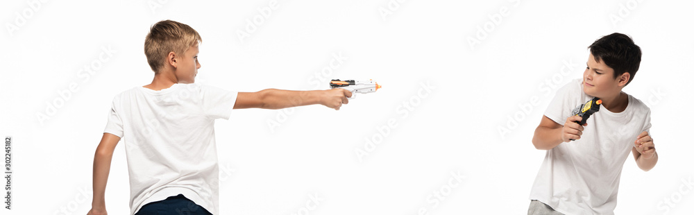 panoramic shot of boy aiming with toy gun at scared brother isolated on white panoramic shot of boy aiming with toy gun at scared brother isolated on white