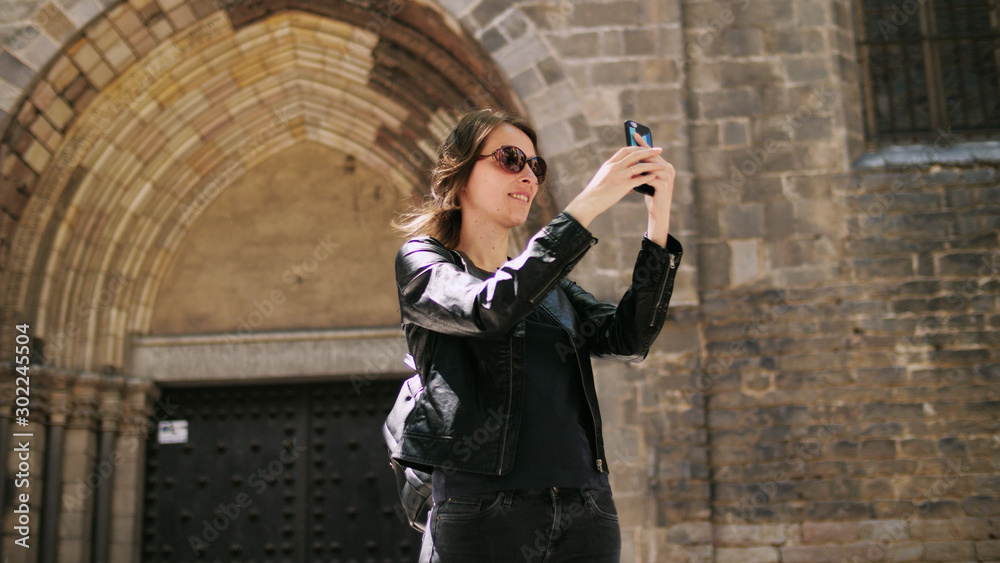 Attractive tourist woman making a selfie uses a smartfone while walking at the street.