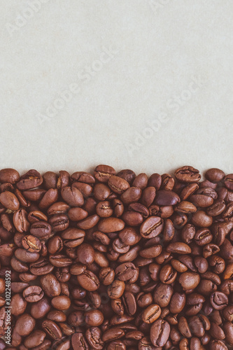 A heap of roasted coffee beans on a neutral paper background with copy space. © tatyana