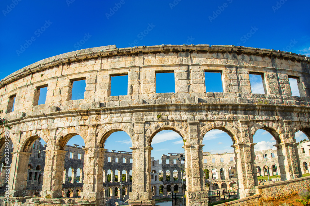 Ancient heritage in Pula, Istria, Croatia. Arches of monumental ancient Roman arena. Detail of historic amphitheater, wide angle view of high walls on blue sky background.