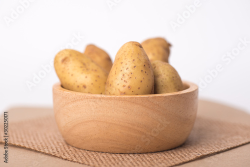 Close up of organic raw potato in a brown wooden bowl on a white background