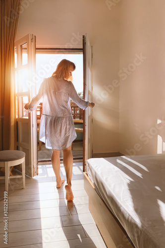 Beautiful young woman standing in doorway at sunset. Back view of sensual lady looking at sunny sky at daytime. Pretty girl enjoying morning sunlight. Female figure at door entrance in sunlit room