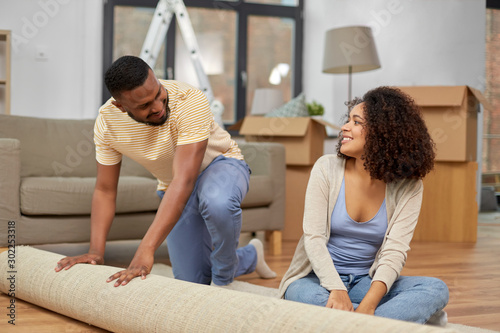 moving, people, repair and real estate concept - happy african american couple with carpet at new home