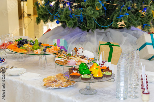 Various fruits, desserts, pastries on the holiday table. New year or Christmas. Decorated Christmas tree.