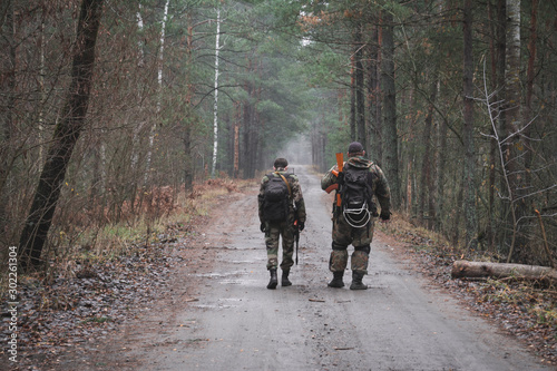 rear view, two soldiers with guns walk along a forest road