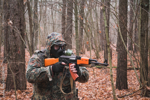 Russian soldier with a gun in his hands and a mask stands in the autumn forest