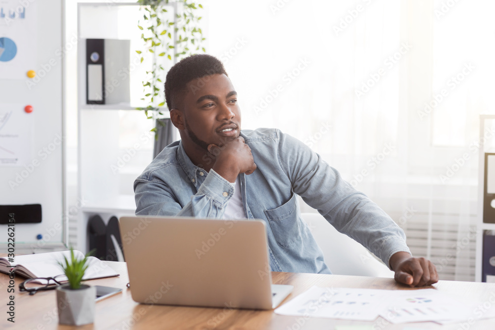 Thoughtful african american employee sitting at workplace in modern office - obrazy, fototapety, plakaty 