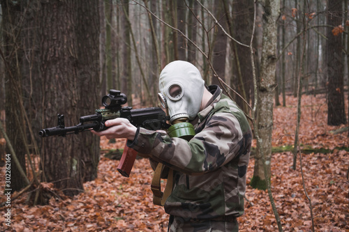 Soldier dressed in ghillie suit, aiming with assault rifle, gas mask face