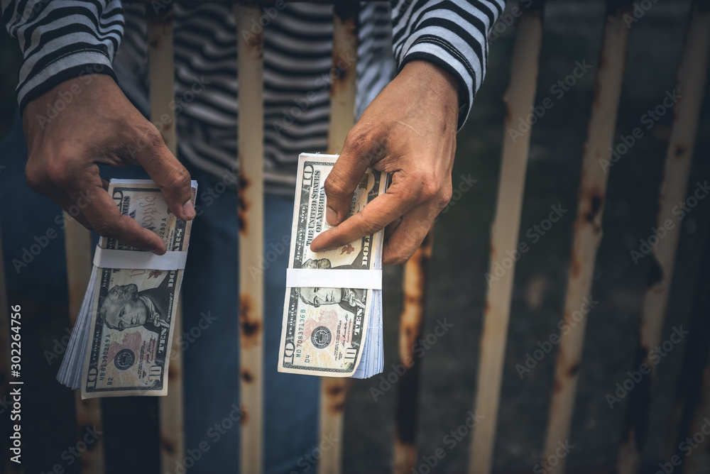 Male criminals Captured in a dirty cage On charges of counterfeiting a bank dollar, in which he held the fake banknote in his hand, to financial crime concept. - obrazy, fototapety, plakaty 