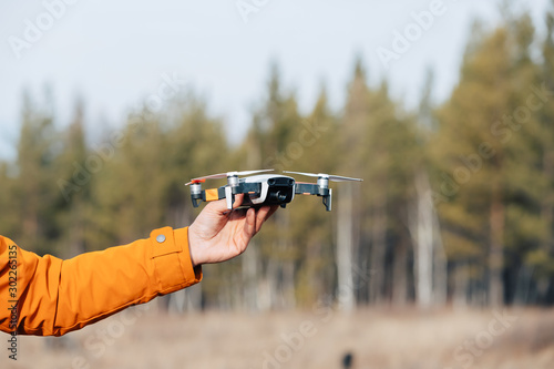 A man in clothes with an orange sleeve holds a flying quadcopter drone in his hand.