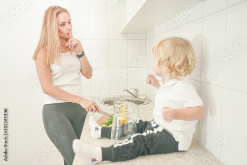 Portrait of an adorable mother and little baby child preparing a vegetable water drink together in the white kitchen