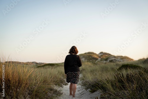 Woman from behind walking on a dune in the golden hour