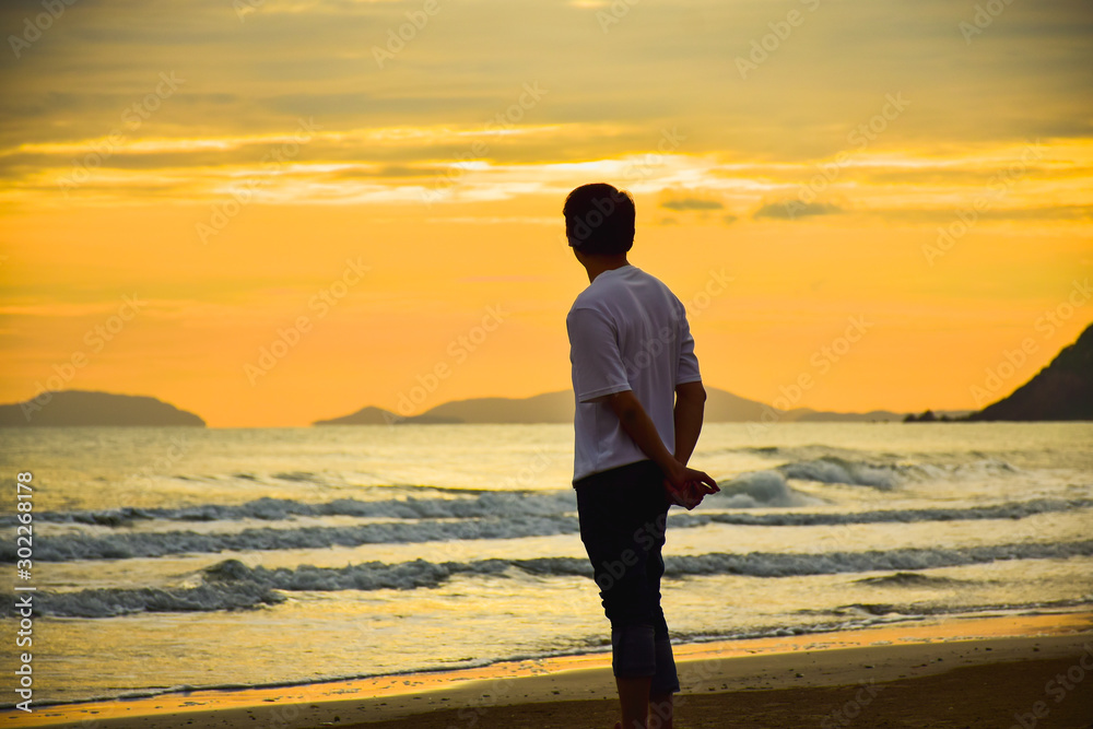 Asian man in white shirt standing alone and look at beautiful sea at twilight.