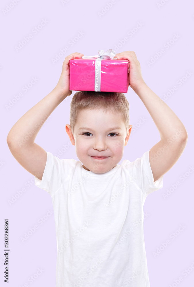 Cute boy with pink gift box in a white T-shirt on color background. Copy space. Christmas and new year concept. Cute boy with pink gift box in a white T-shirt on color background. Copy space. Christmas and new year concept.