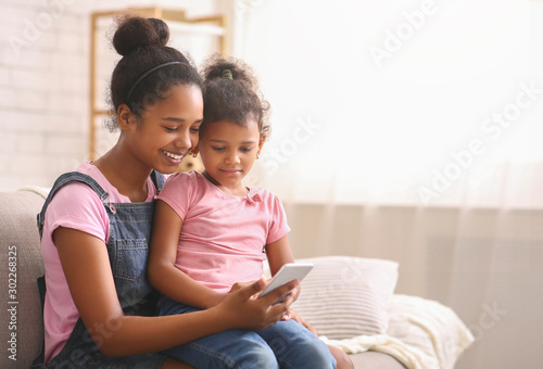 Teen and little african american sisters browsing on cellphone