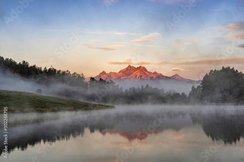 Peaceful mountain scene with calm lake, colorful trees and high peaks in a golden warm light. Scenic view of High Tatras National Park, Slovakia.