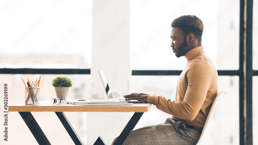 Afro businessman working on laptop in modern office, side view