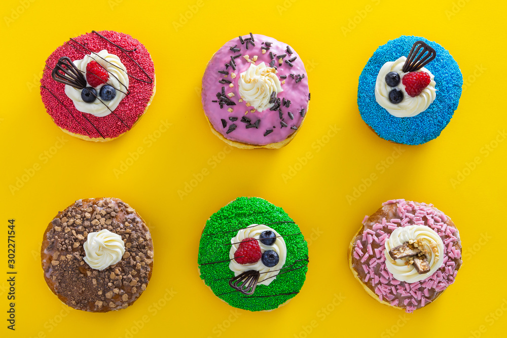 various donuts with sweet topping on yellow background top view