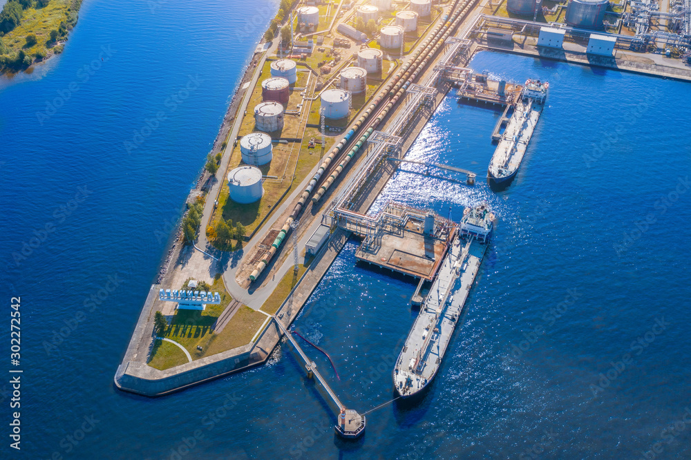 Aerial view large port oil loading terminal with large storage tanks. Railway infrastructure for the delivery of bulk cargo by sea, using pump station in ship tanker for transportation and delivery.