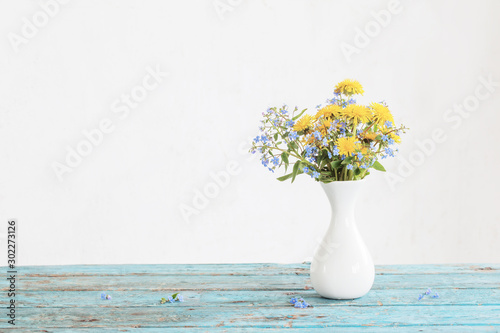 dandelions and forget-me-not in vase on background old wall