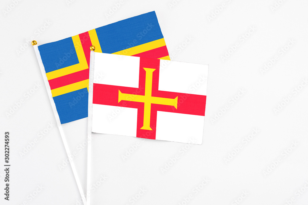 Guernsey and Aland Islands stick flags on white background. High quality fabric, miniature national flag. Peaceful global concept.White floor for copy space.