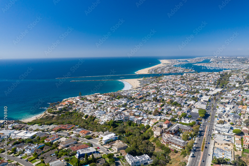 Aerial view over Newport Beach in Orange County, California with coastal neighborhood and homes below on a sunny blue sky day.